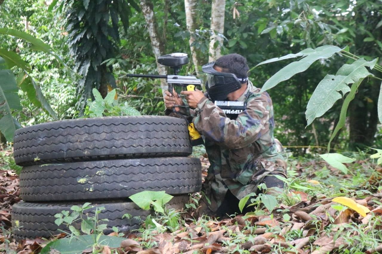 Paintball player in camouflage aiming from behind tires in jungle